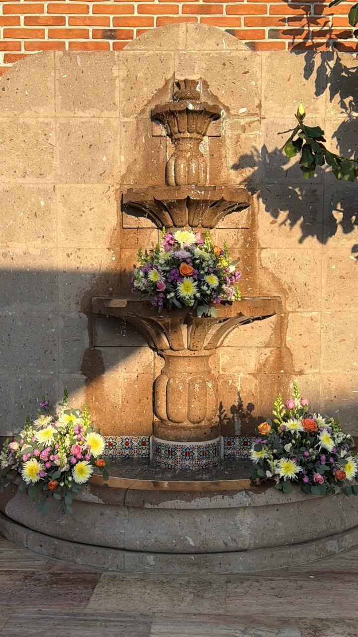 Fuente de cantera adornada con arreglos florales al pie, en la hora dorada