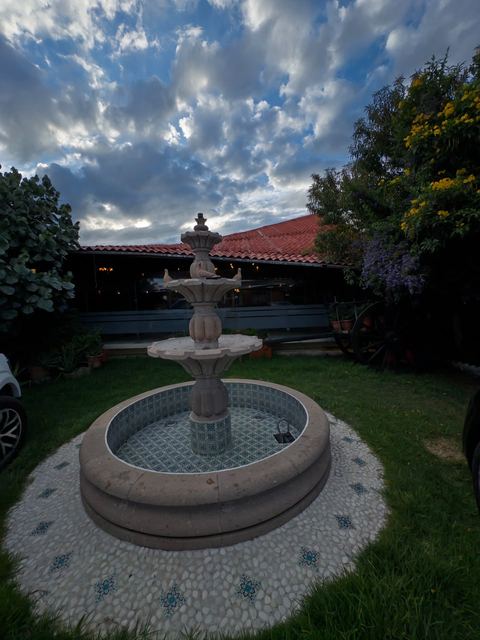 Fuente de cantera con talavera en el jardín, rodeada de pasto y jardineras