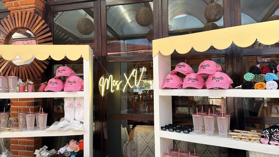 Mesa de recuerdos de unos XV años, con letrero de neón, gorras y vasos personalizados