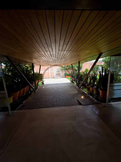 Pórtico techado de acceso, con piso empedrado, rampa y plantas a los lados
