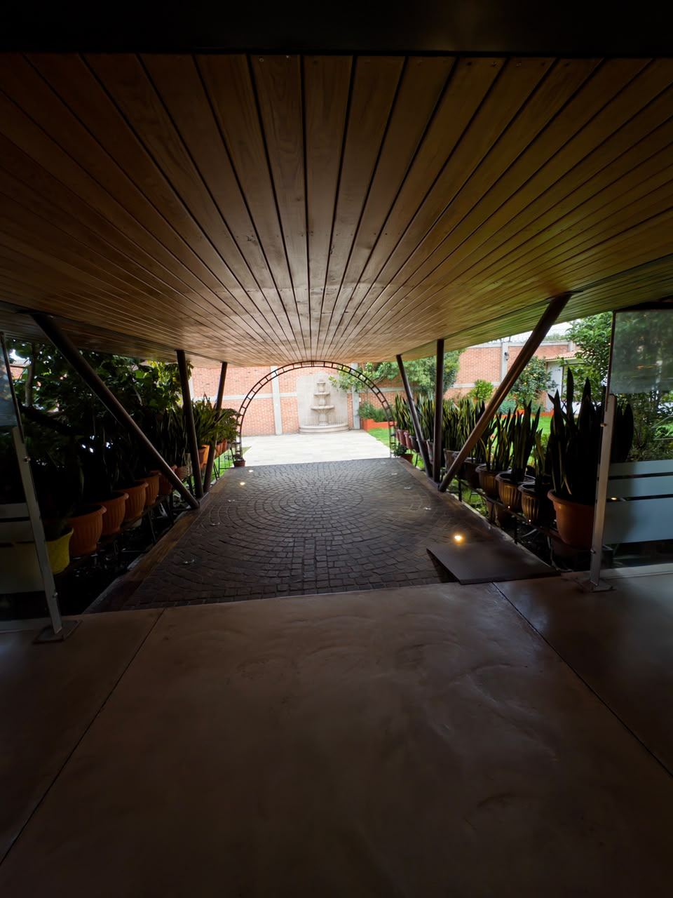 Pórtico techado de acceso, con piso empedrado, rampa y plantas a los lados